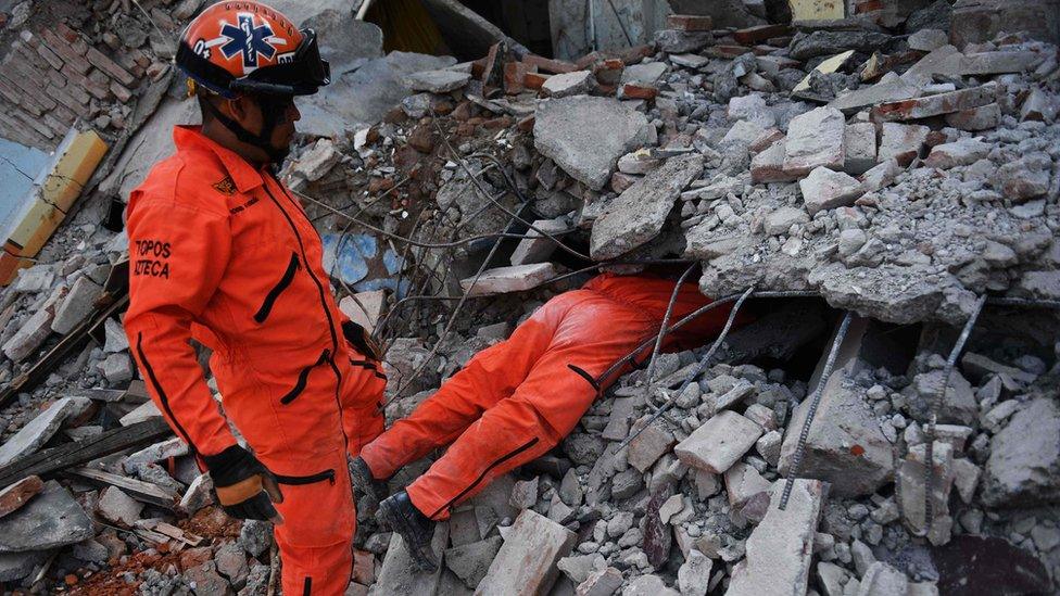 Man in jumpsuit with top half of his body under rubble