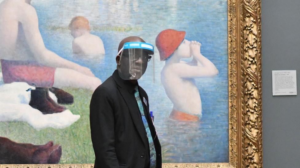 A member of staff wearing a protective face shield walks past "Bathers at Asnieres" by Georges Seurat inside the National Gallery in July 2020