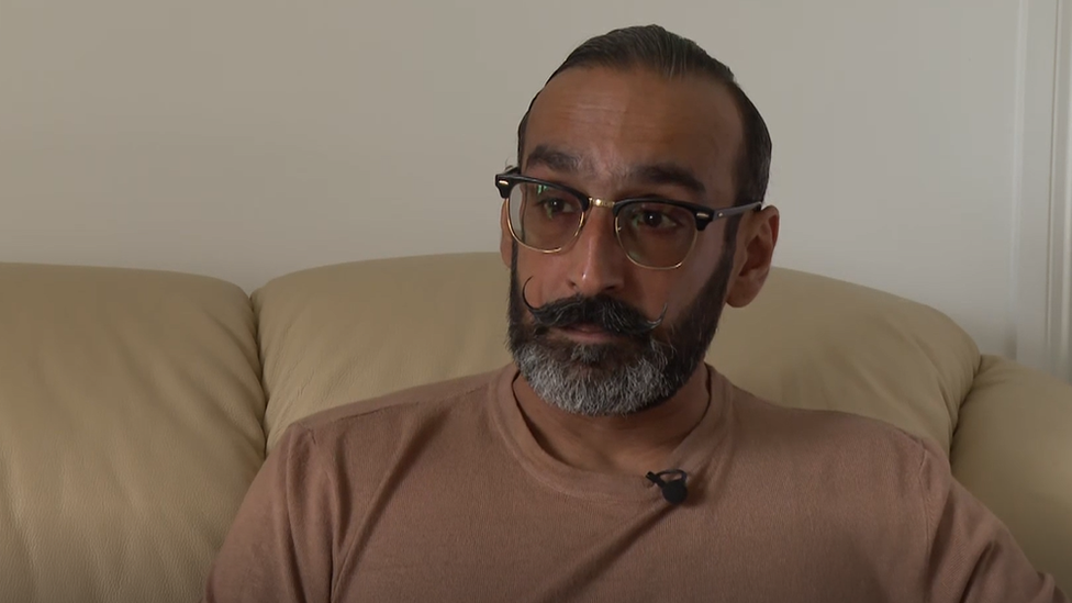 A man wearing a pink t-shirt with tears in his eyes