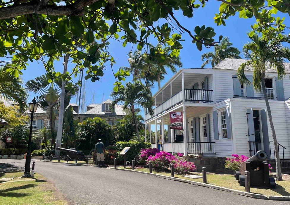 A picture from the area shows a white building, a cannon, lush green foliage and blue skies