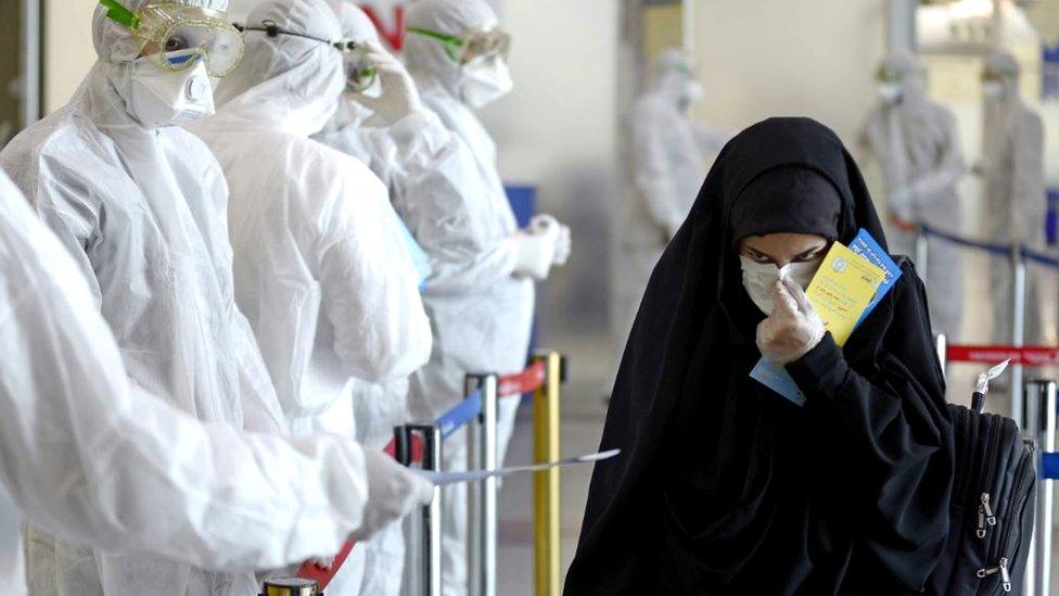 Medical staff in protective gear distribute leaflets to Iraqi passengers returning from Iran, 5 March 2020