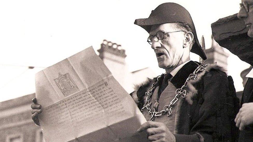 Two men in formal gowns and headwear read a large document in 1952