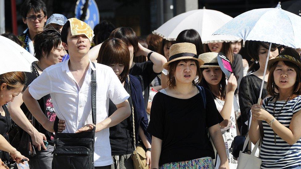 People wait to cross the road as they use umbrellas and hats to shade themselves from the sun in Tokyo