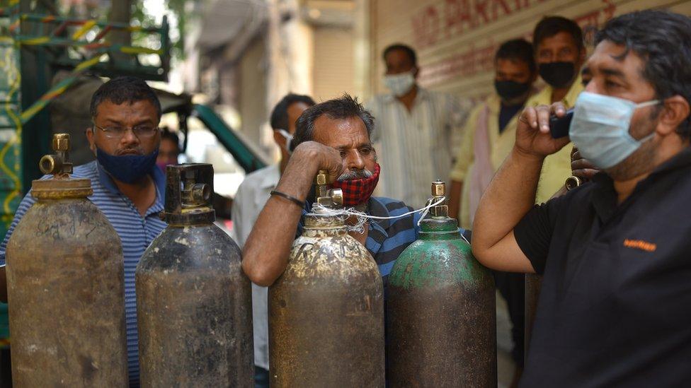 People wait to fill their oxygen cylinders at an oxygen vendor in New Delhi