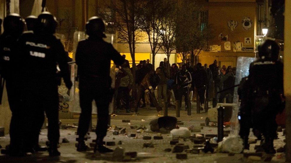 A line of Spanish national police officers face a line of protesters in the street after dark in Madrid