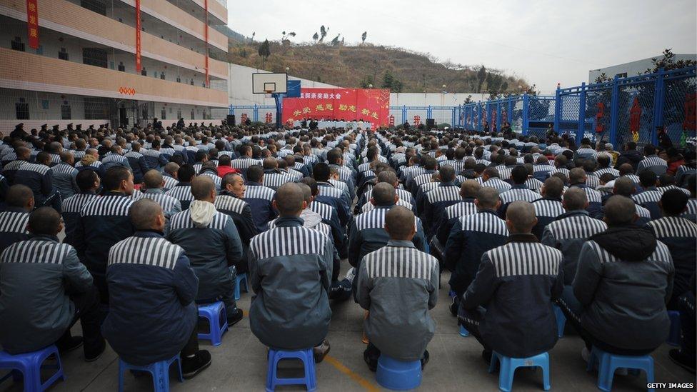 Prisoners sitting in rows in a prison yard for an event