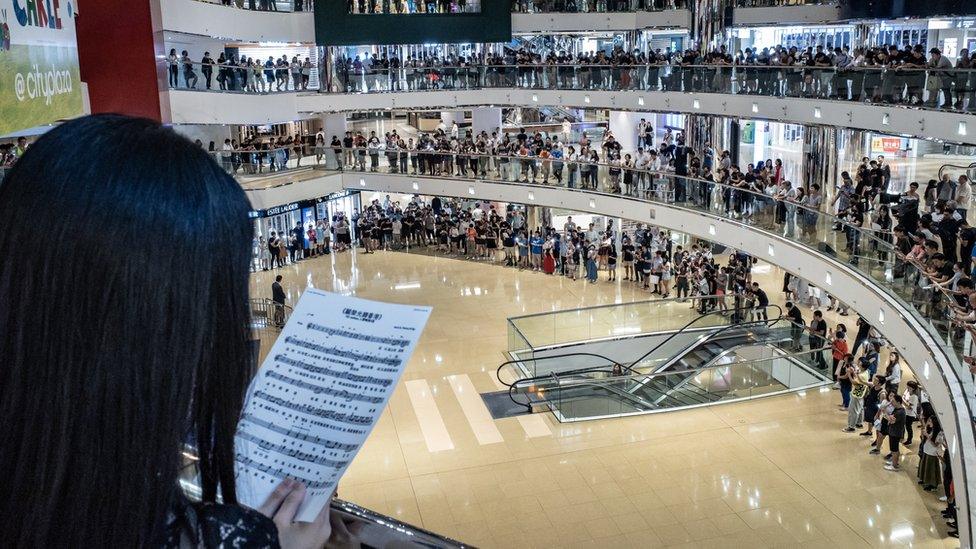 Residents and protesters sing songs and shout slogans as they gather at a shopping mall after business hours in Tai Koo district