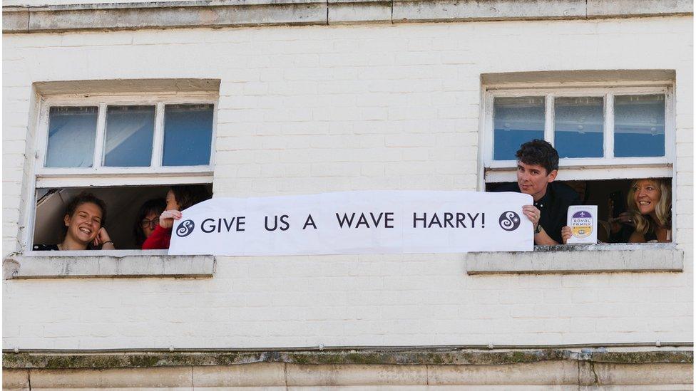 Well-wishers hold a banner saying "Give us a wave, Harry"