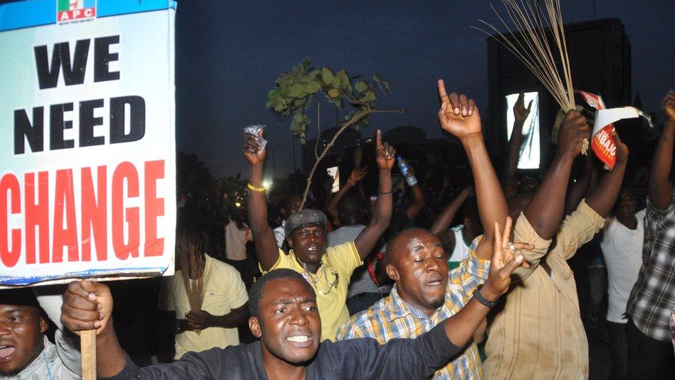 People holding a placard saying 'We Need Change'