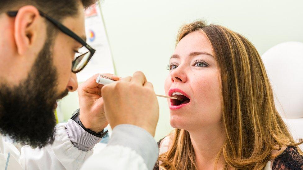 Lady having her throat checked by a male doctor / pharmacist