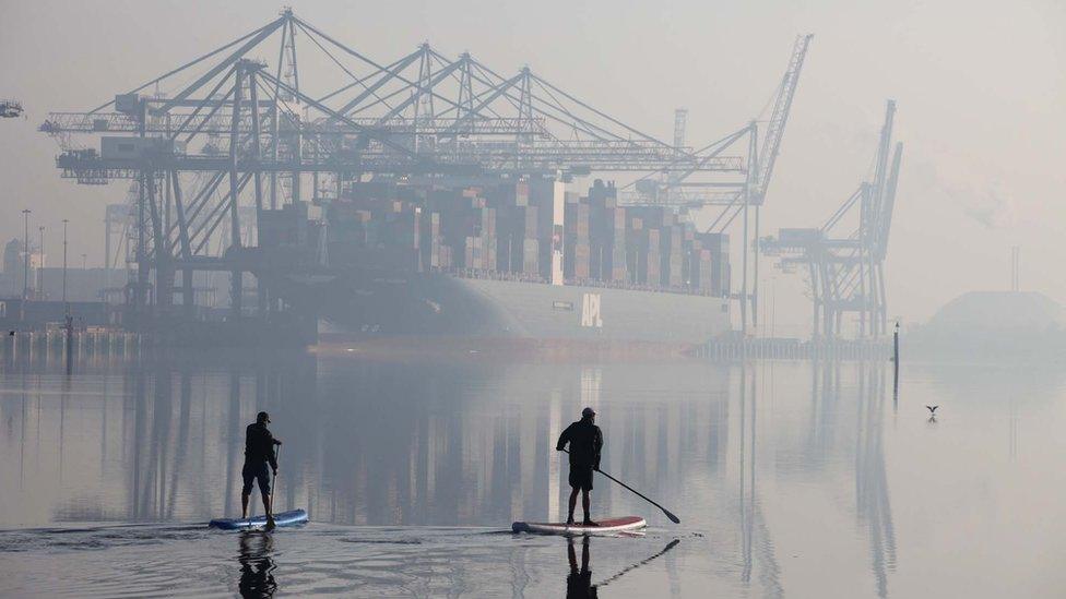 Two paddle boarders passing in front of a container ship at Southampton Docks in Hampshire