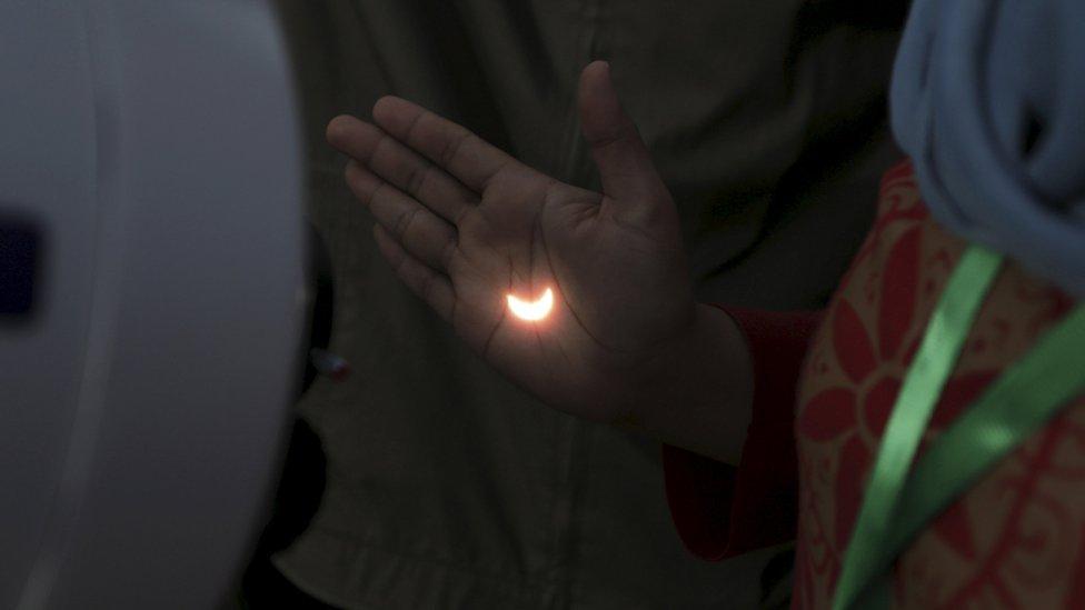 The reflection of the partial eclipse seen on a woman's hand.