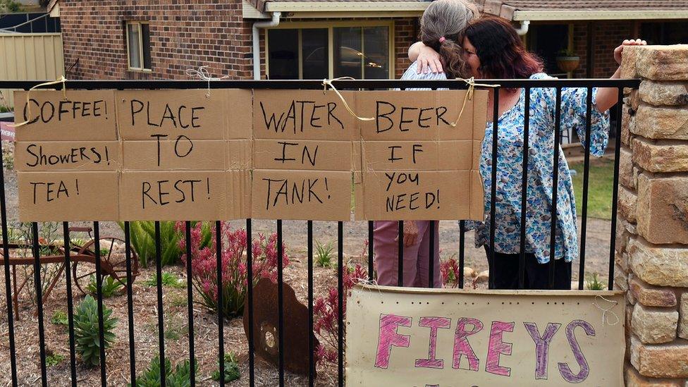 Neighbours in Nana Glen embrace outside their homes after returning after the bushfire