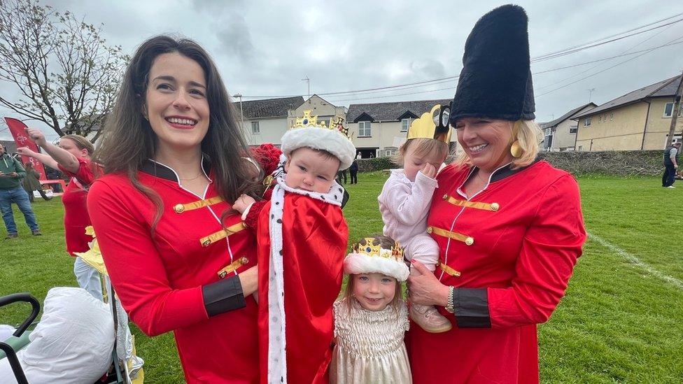 two women and three children, including a baby with a crown, dressed up on royal regalia