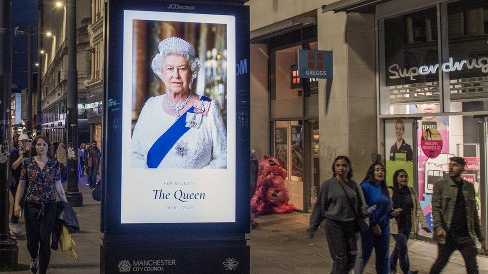 A digital advertising board in Piccadilly Gardens shows an image of Queen Elizabeth II