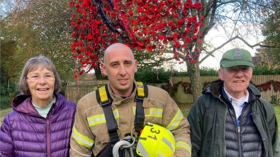 Organisers Sandra and Jimmy, and firefighter David Ion in uniform, standing in front of the poppies