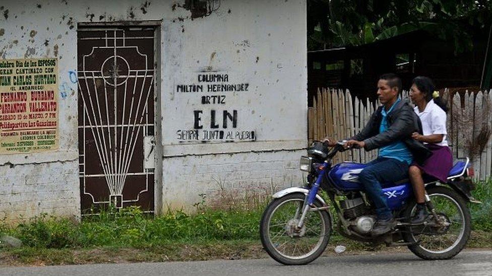 A couple ride a motorcycle past a graffiti of the ELN (National Liberation Army of Colombia) guerrillas on a wall in El Palo, department of Cauca, Colombia, on March 15, 2016.