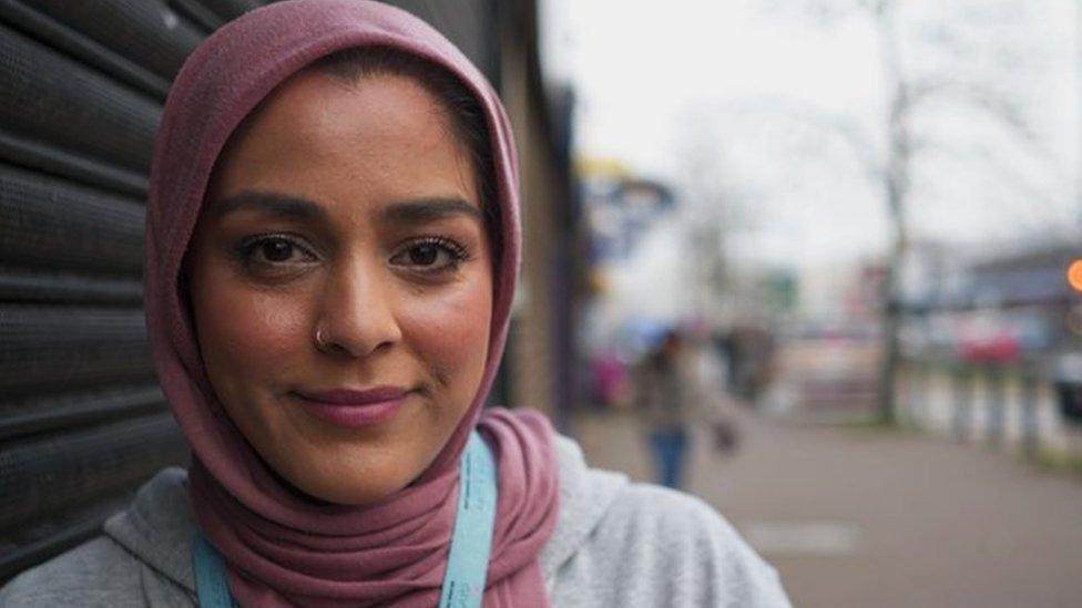 Hana, a young woman wearing a hijab and lanyard, outside a shop on a road in Leeds