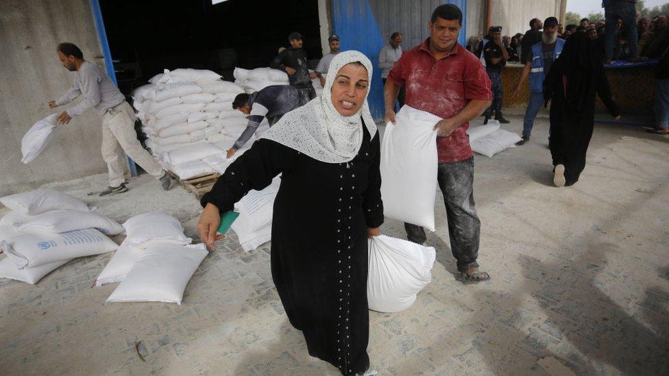 A woman drags a large bag of flour away as Unrwa workers distribute it to Gazans