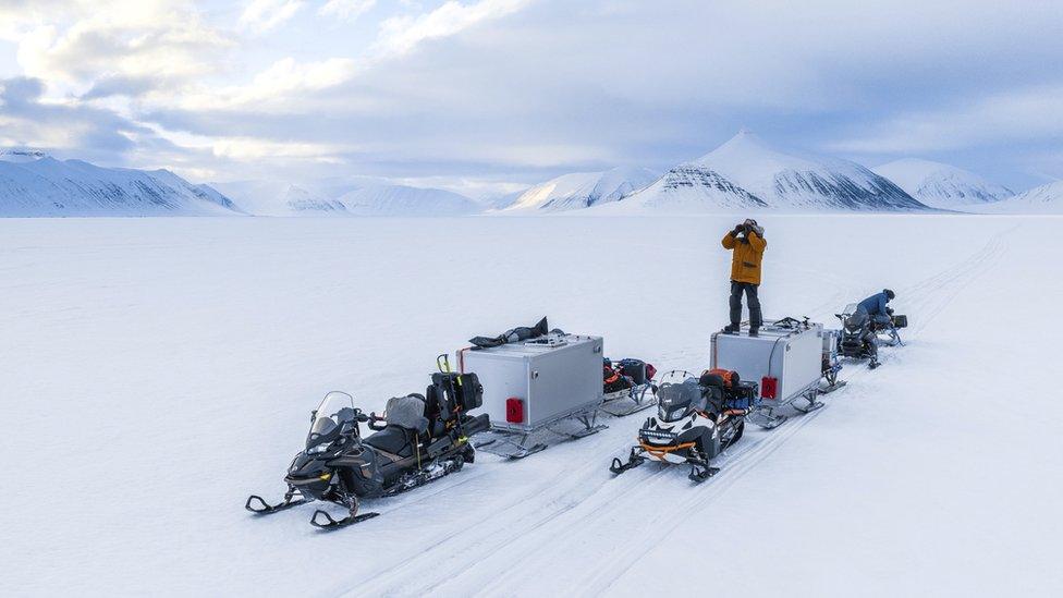 BBC crew member searches the horizon for polar bears in Svalbard, Norway. Standing on a two-person 'sleeping pod' built specially - to allow the film crew to remain with the polar bears around the clock.