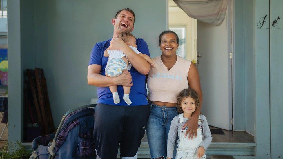 Daniela, Rafael and their two young children stand in front of their tiny house