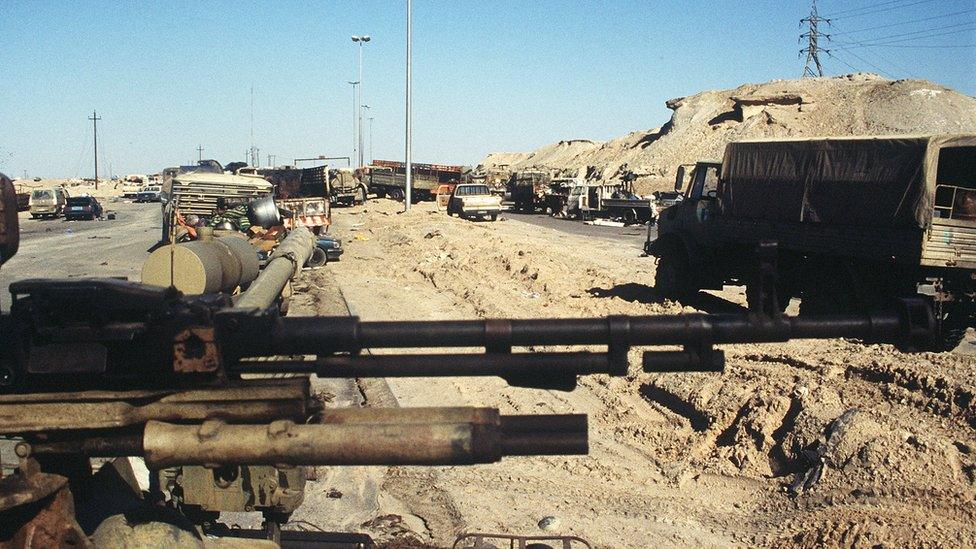 Abandoned cars and trucks clog the road leading out of Kuwait City after the retreat of Iraqi forces from the city. In the foreground is an Iraqi anti-aircraft gun, damaged in one of the final attacks by Coalition forces during Operation Desert Storm