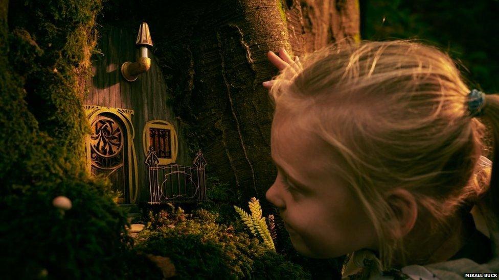 close up of girl looking at miniature home in woods