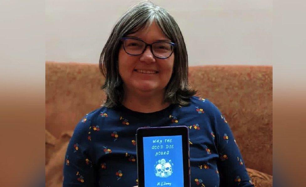 Clare Fayer holding a kindle displaying Mckenzy's novel Why the Good Die Young