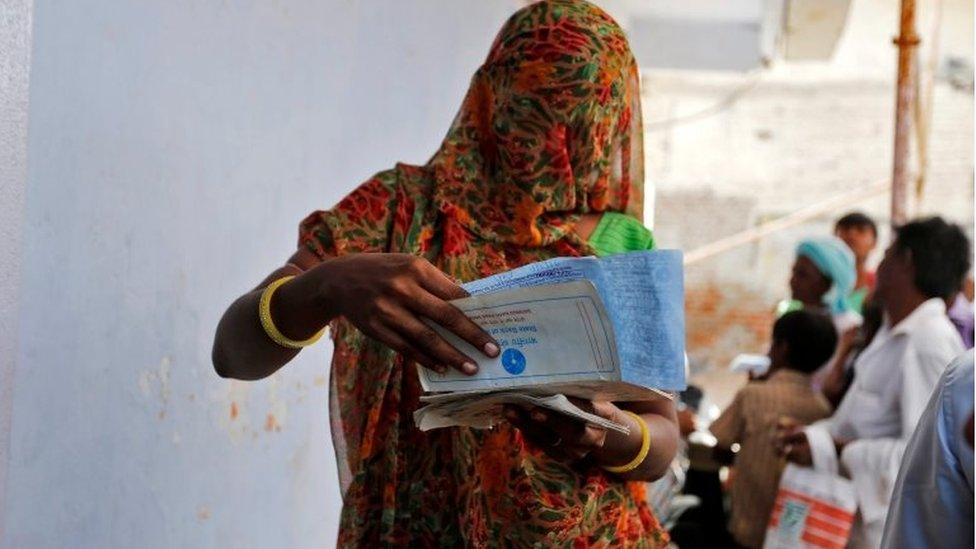 A woman checks her documents before depositing her old, high denomination banknotes outside a bank in Khoraj village on the outskirts of Ahmedabad