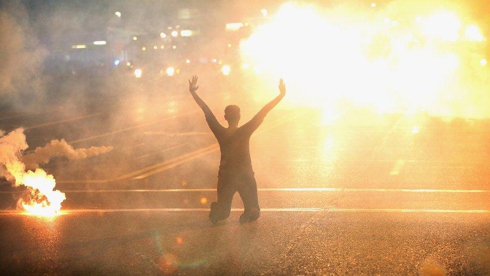 Tear gas reigns down on a woman kneeling in the street with her hands in the air after a demonstration over the killing of teenager Michael Brown by a Ferguson police officer