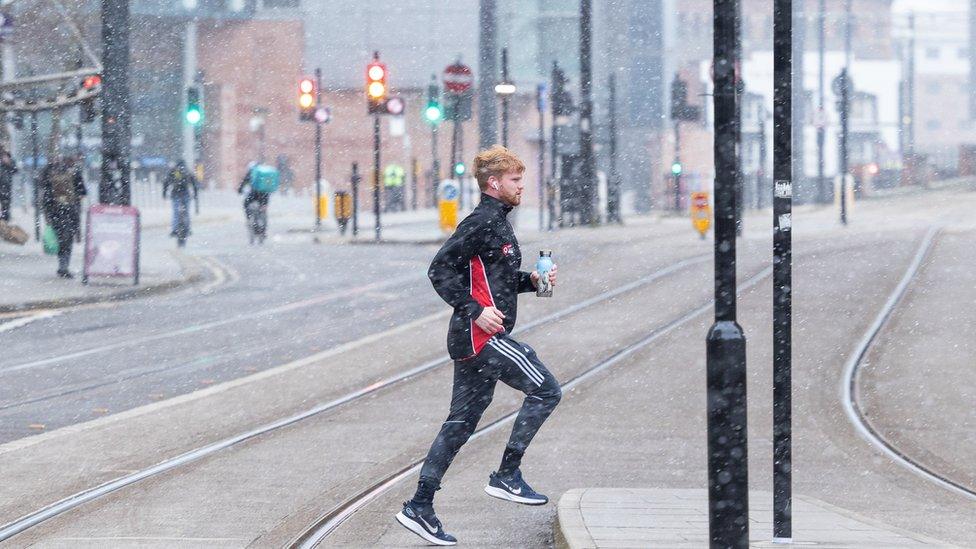 A man running in snowfall in Manchester city centre