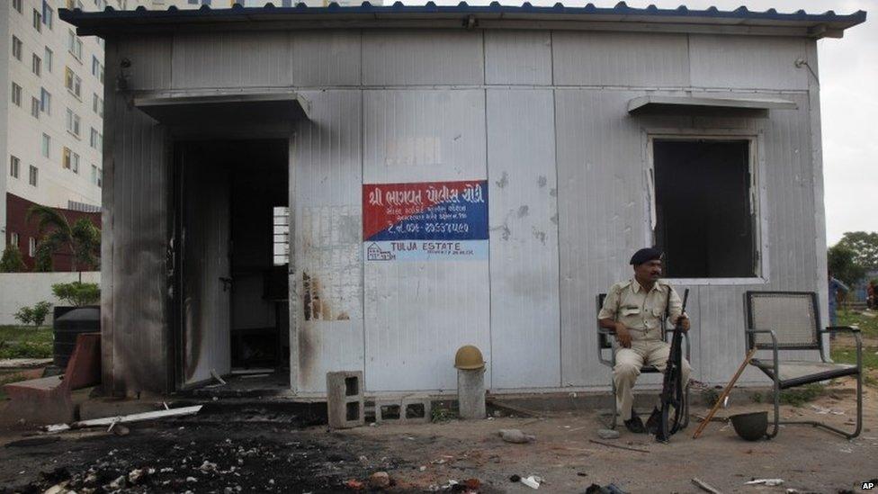 An Indian policeman sits outside a damaged police post that was set on fire during clashes in Ahmadabad, India, Wednesday, Aug. 26, 2015