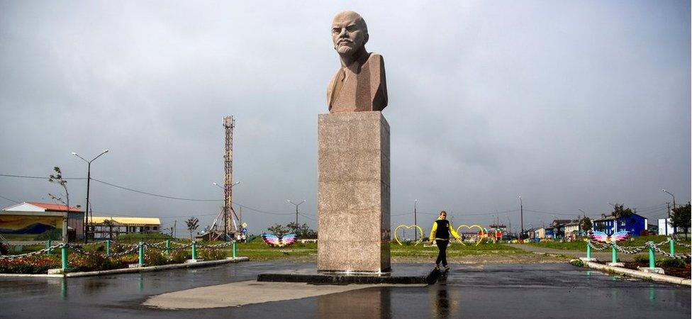 A woman walks past a Lenin statue in Yuzhno-Kurilsk, the main settlement on the southern Kuril island of Kunashir, 7 September 2015.