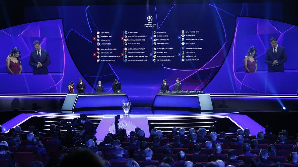 uefa draw with the groups displayed on a screen behind uefa officials