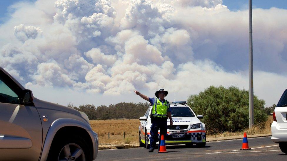 Smoke clouds from a large bush fire are seen behind a police road block at the turn off onto the South Western Highway near Pinjarra, Western Australia