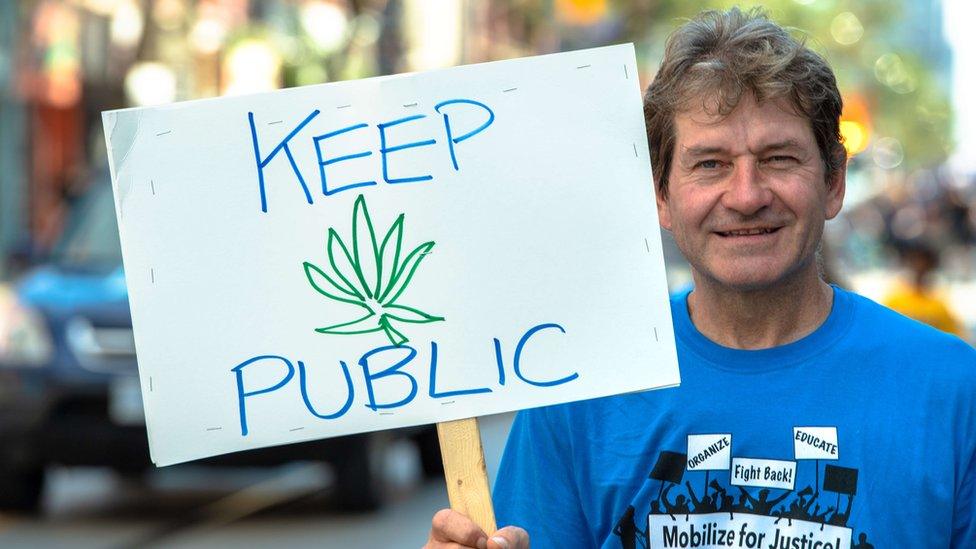 A man holds up a protests sign urging cannabis to be kept public