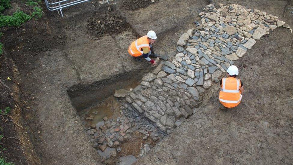 Archaeologists cleaning a paved entry way into the moat