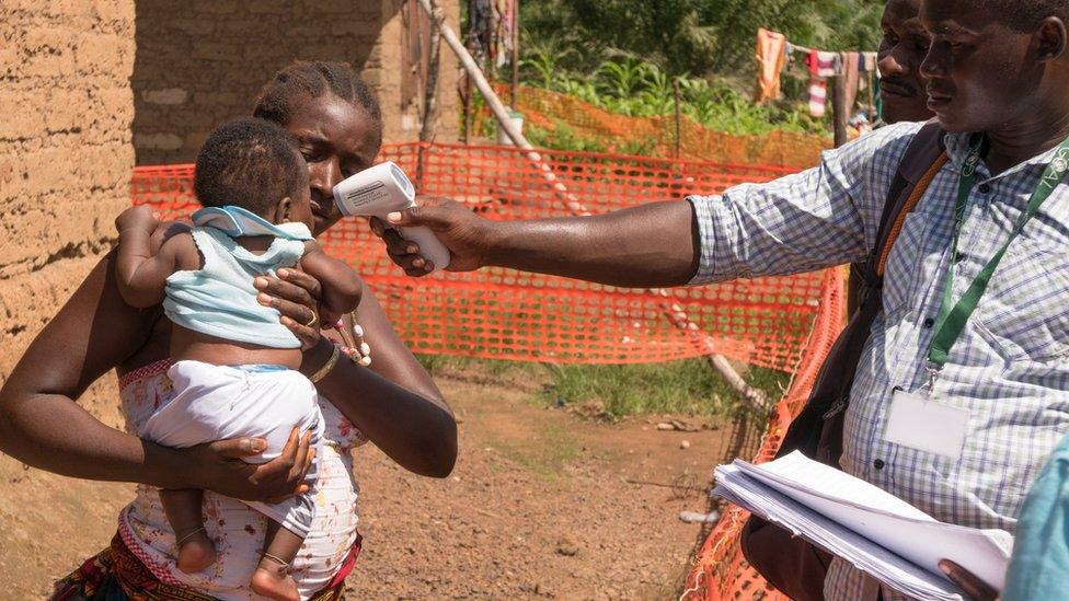 A baby is checked for symptoms by a community investigator