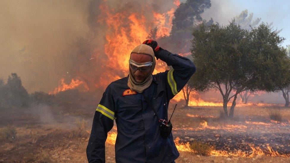 A firefighter stands in front of a wildfire in Rhodes