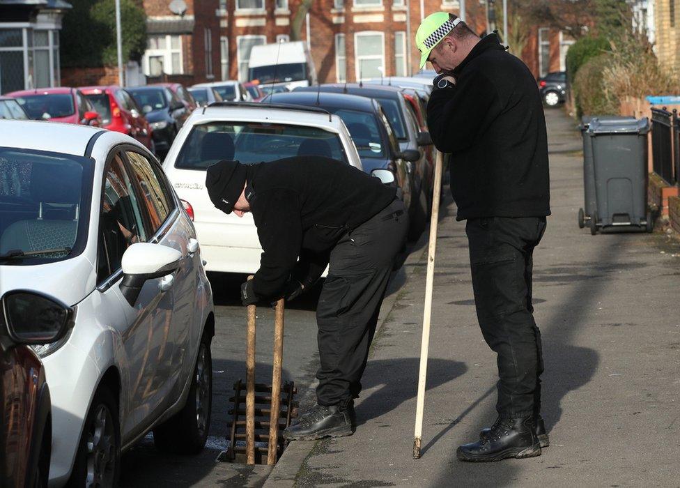 Two men looking into a drain on the roadside