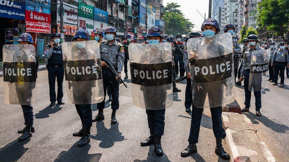 Riot police stand guard as anti-coup protesters march through the streets in Yangon, Myanmar