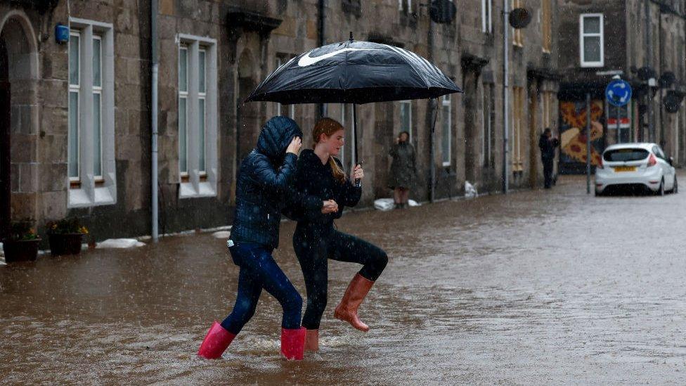 Two people crossing a flooded road in Dumbarton in Scotland