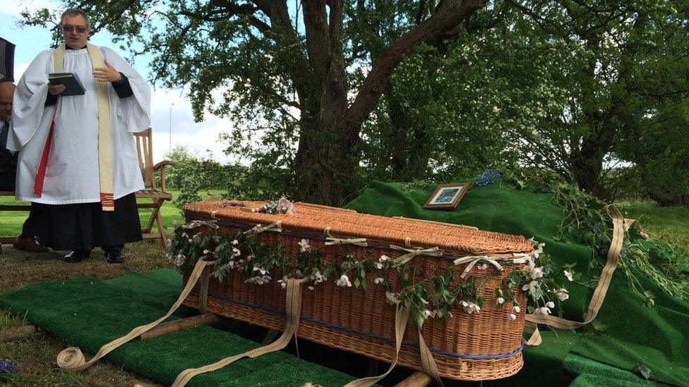 A wicker coffin being buried in woodland