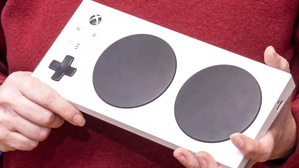 This close-up shot of a Xbox adaptive controller being held shows the white rectangle, dominated by two large circular buttons - with extra ports for add-ons on the side