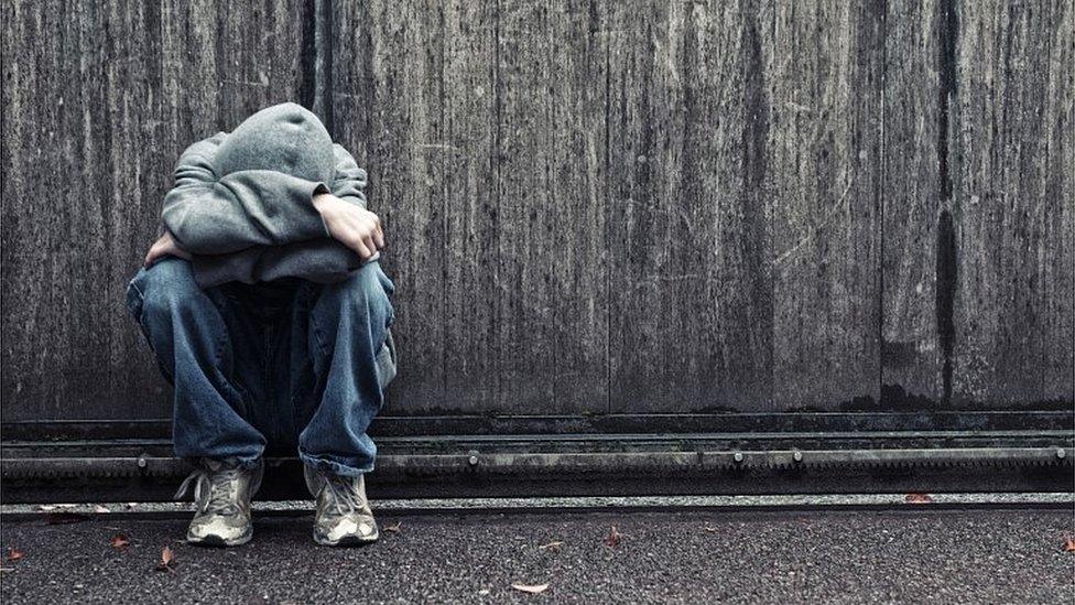 Teenager covering their face with hands and a hood