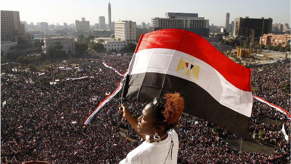 A woman waves an Egyptian flag overlooking crowds in Tahrir Square, Cairo (Feb 2011)