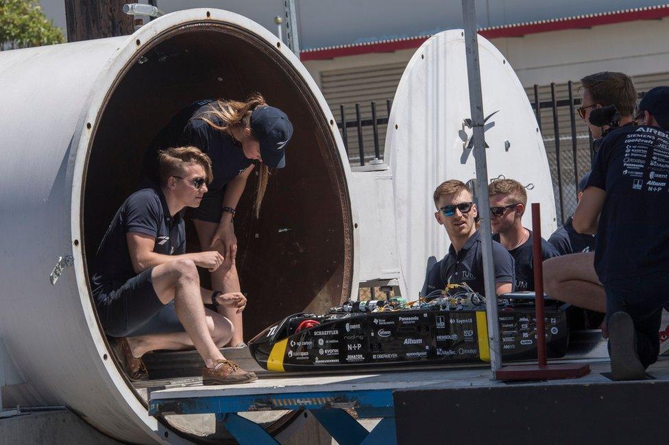 A handful of students sit in the mouth of a SpaceX tunnel with their pod