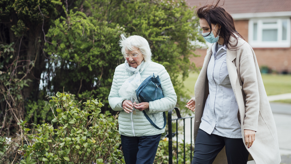 A younger woman wearing a mask walking with an older woman