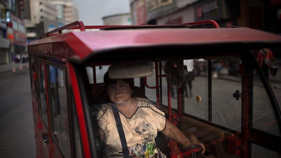 A woman drives her tuk tuk (taxi) looking for customers in a street in Zhengzhou, China