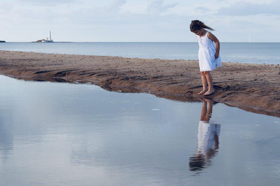 A girl looks at her reflection in a calm lagoon next to the sea